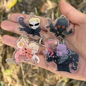 May include: Four acrylic keychains featuring cartoon characters. One keychain depicts a character with sunglasses and a black outfit. Another shows a character in a gas mask holding a gun. The other two keychains show characters with mutated features.