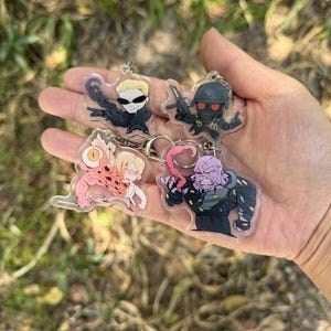 May include: Four acrylic keychains featuring cartoon characters. Each keychain has a different character design, including a character with sunglasses, a soldier with a helmet, a character with a mutated body, and a purple-skinned character.