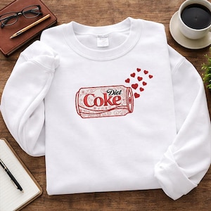 May include: White sweatshirt featuring a red and white Diet Coke can design with red heart accents. The sweatshirt has a crew neck and long sleeves. The Diet Coke can design includes the text "Diet Coke".