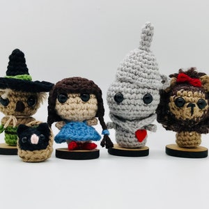 Puede incluir: Cinco personajes de crochet del Mago de Oz: el Espantapájaros, Dorothy, el Hombre de Hojalata, el León Cobarde y Toto el perro. Los personajes están todos de pie sobre pequeñas bases de madera.