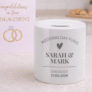 May include: A white ceramic mug with a black handle and the text "But First, Coffee" in a black, handwritten-style font. The mug is on a white surface.