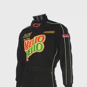 Puede incluir: Traje de carreras negro con el logo "Mello Yello" en rojo y verde. El traje tiene detalles en amarillo neón, un logotipo de Chevrolet y un parche "Simpson". También es visible el logotipo de NASCAR.