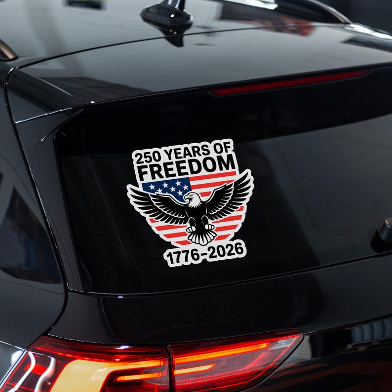 K&ouml;nnte beinhalten: Ein wei&szlig;er Aufkleber mit dem Text "250 YEARS OF FREEDOM" &uuml;ber einem Design der amerikanischen Flagge und einem Wei&szlig;kopfseeadler. Der Aufkleber enth&auml;lt auch die Daten "1776-2026". Der Aufkleber ist auf der Heckscheibe eines schwarzen Fahrzeugs angebracht.