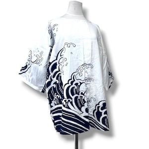 May include: A white short-sleeved shirt featuring a bold navy blue graphic print of stylised ocean waves. The garment has a wide, loose-fitting silhouette with a round neckline, showcasing a repeating wave pattern across the front and sleeves.