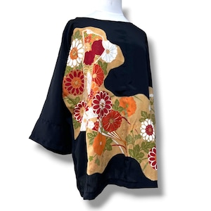 May include: A black long-sleeved top featuring a large, asymmetrical tan panel on the front. The panel is decorated with a vibrant floral pattern of red, orange, and white chrysanthemums with green leaves. The garment has a wide, loose fit.