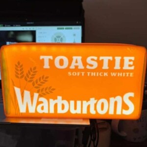 May include: An orange sign with the word "TOASTIE" in white, along with "SOFT THICK WHITE" and the brand name "Warburtons". The sign also features a wheat graphic.