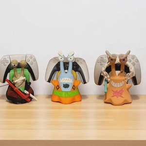 Op de afbeelding: Vijf kleurrijke, gestileerde figuren, elk met een PlayStation 5-controller als achtergrond. De figuren hebben unieke ontwerpen, waaronder een personage met een rode hoed en een personage met een groene outfit.