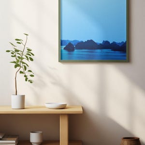 Blue-toned photograph of Ha Long Bay with coastal limestone islets reflected in calm water.
