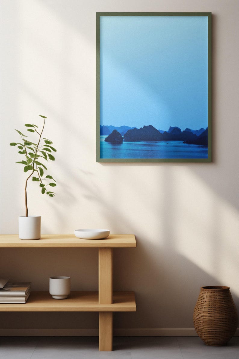 Blue-toned photograph of Ha Long Bay with coastal limestone islets reflected in calm water.