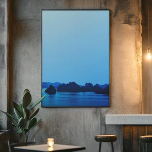 Blue-toned photograph of Ha Long Bay with coastal limestone islets reflected in calm water.