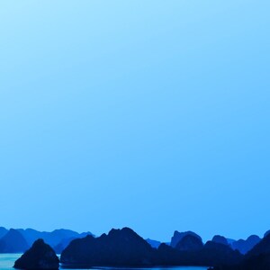 Blue-toned photograph of Ha Long Bay with coastal limestone islets reflected in calm water.