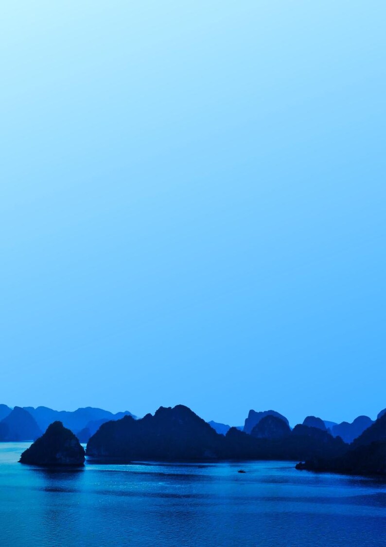 Blue-toned photograph of Ha Long Bay with coastal limestone islets reflected in calm water.