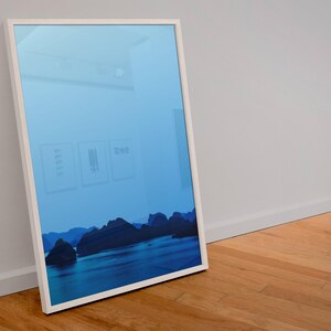 Blue-toned photograph of Ha Long Bay with coastal limestone islets reflected in calm water.