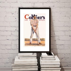 May include: Framed vintage print of a golfer from Collier's magazine. The artwork features a man in a light pink shirt and white pants, poised to swing a golf club. The magazine title is in red and black.