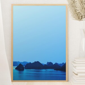 Blue-toned photograph of Ha Long Bay with coastal limestone islets reflected in calm water.