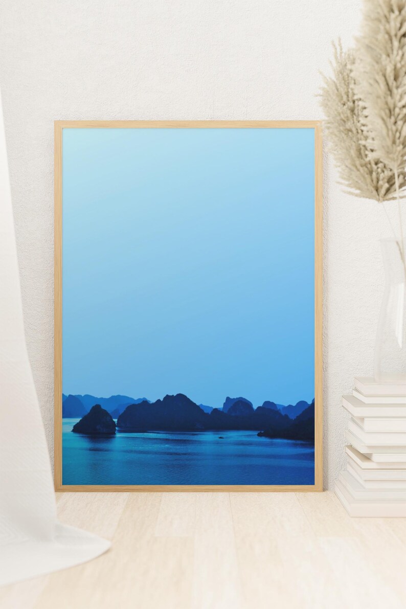 Blue-toned photograph of Ha Long Bay with coastal limestone islets reflected in calm water.