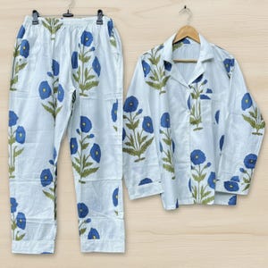May include: White pajama set with a blue floral pattern. The set includes a button-down shirt and matching pants. The floral design features blue flowers with green leaves and stems.