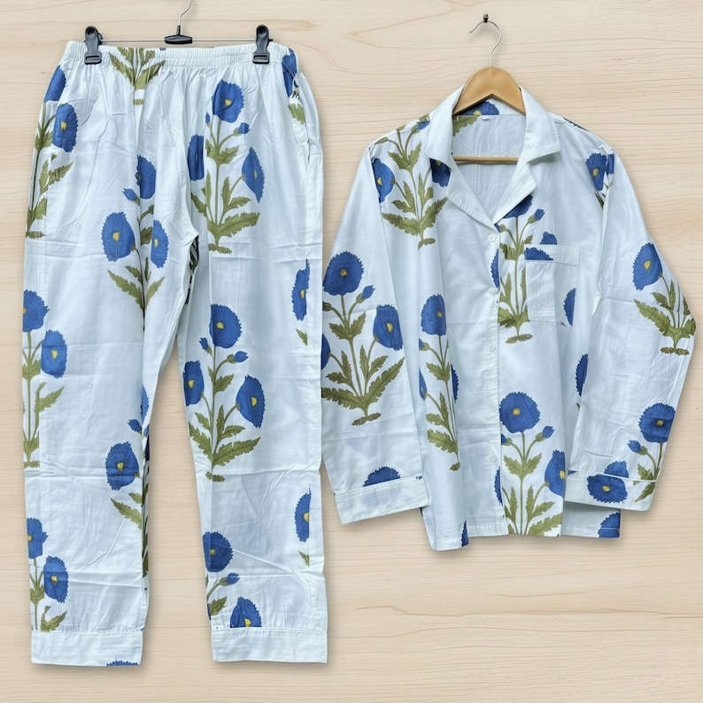 May include: White pajama set with a blue floral pattern. The set includes a button-down shirt and matching pants. The floral design features blue flowers with green leaves and stems.