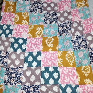 May include: A patchwork quilt with a variety of floral and paisley patterns in shades of pink, teal, mustard yellow, and navy blue. The quilt is made of square fabric pieces sewn together, creating a vibrant and colorful design.