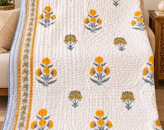 May include: A white quilted blanket featuring a repeating pattern of yellow flowers with gray stems and leaves. The border consists of a yellow floral vine motif framed by thin blue and white striped edges on all sides of the fabric.