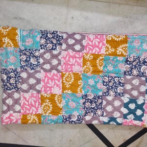 May include: A patchwork quilt featuring a variety of floral and paisley patterns in squares. The quilt's colors include mustard yellow, pink, teal, navy blue, and lavender. The quilt is made of soft fabric and is likely handmade.