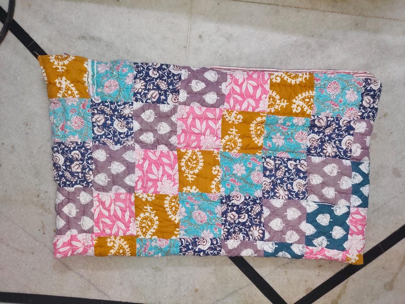 May include: A patchwork quilt featuring a variety of floral and paisley patterns in squares. The quilt's colors include mustard yellow, pink, teal, navy blue, and lavender. The quilt is made of soft fabric and is likely handmade.