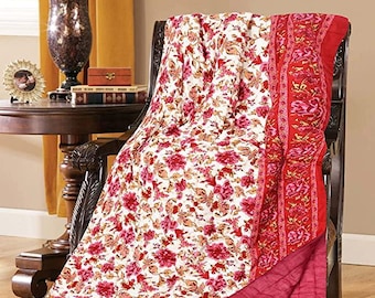 May include: A floral patterned quilt draped over a dark wooden chair. The quilt features a white background with red and pink flowers. The border is red with a floral design. The underside is a solid red color.