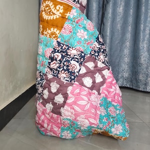 May include: A colorful patchwork quilt with floral and paisley patterns in shades of pink, teal, navy, and mustard. The quilt is folded and appears to be made of cotton fabric. The design features a variety of shapes and sizes.