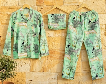 May include: A mint green pajama set with a jungle animal print. The set includes a button-down shirt, shorts, and pants. The print features zebras, leopards, toucans, and palm trees. The pajamas are hanging on wooden hangers against a textured wall.