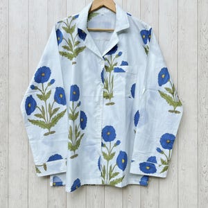 May include: White pajama set with a blue floral pattern. The long-sleeved top has a button-down front and a chest pocket. The floral design features blue flowers and green leaves.