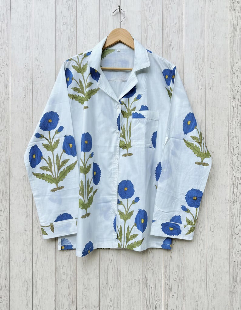 May include: White pajama set with a blue floral pattern. The long-sleeved top has a button-down front and a chest pocket. The floral design features blue flowers and green leaves.