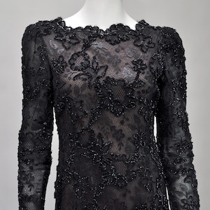May include: Black lace dress with long sleeves and floral embroidery. The dress features a round neckline and is displayed on a mannequin. The intricate lace design is embellished with small, sparkling beads, creating a formal and elegant look.