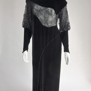 Puede incluir: Vestido de noche de terciopelo negro sobre un maniqu&iacute;. El vestido presenta mangas largas y una superposici&oacute;n de lentejuelas en el corpi&ntilde;o y las mangas superiores. Una costura diagonal recorre el frente.