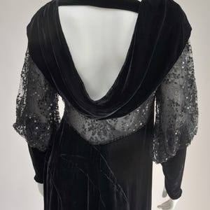 Puede incluir: Vestido largo de terciopelo negro con cuello vuelto y espalda abierta. El vestido de manga larga presenta paneles de encaje transparente con adornos de lentejuelas en las mangas y el corpi&ntilde;o. El vestido tiene una silueta fluida.