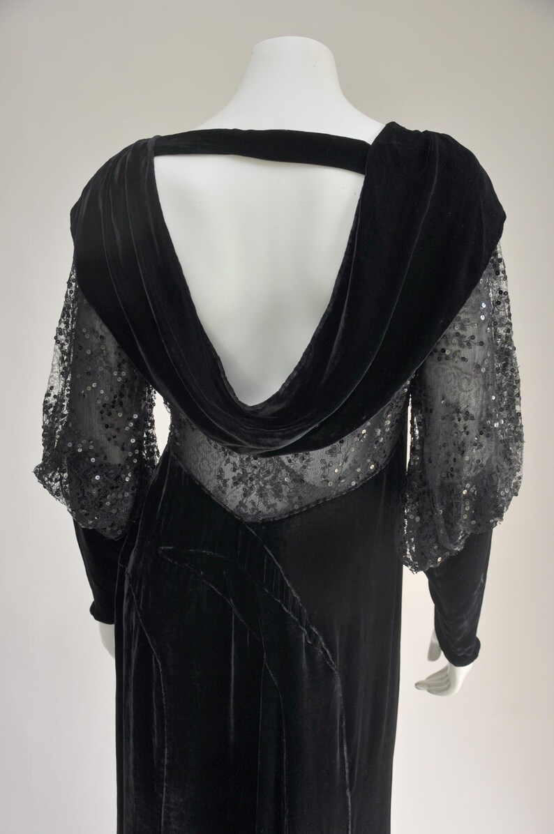 Puede incluir: Vestido largo de terciopelo negro con cuello vuelto y espalda abierta. El vestido de manga larga presenta paneles de encaje transparente con adornos de lentejuelas en las mangas y el corpi&ntilde;o. El vestido tiene una silueta fluida.