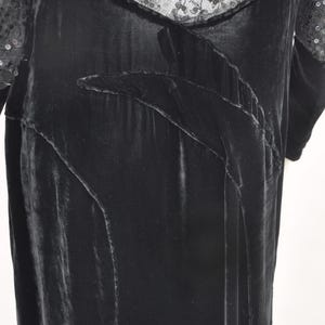 Puede incluir: Un vestido de terciopelo negro con escote y mangas de encaje con lentejuelas. El vestido presenta un dise&ntilde;o fluido con paneles decorativos y una textura suave y lujosa. Las mangas largas est&aacute;n adornadas con lentejuelas, a&ntilde;adiendo un toque de brillo.
