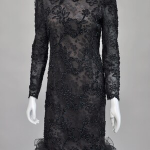 May include: Black lace dress with long sleeves and a ruffled hem. The dress features intricate floral embroidery and beadwork throughout. The neckline is scalloped, and the dress is displayed on a mannequin.