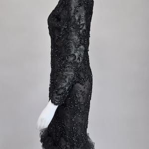 May include: A black, long-sleeved dress with intricate floral lace detailing. The dress features a fitted silhouette and a ruffled hemline. The fabric is embellished with small, sparkling accents, adding a touch of glamour to the formal attire.