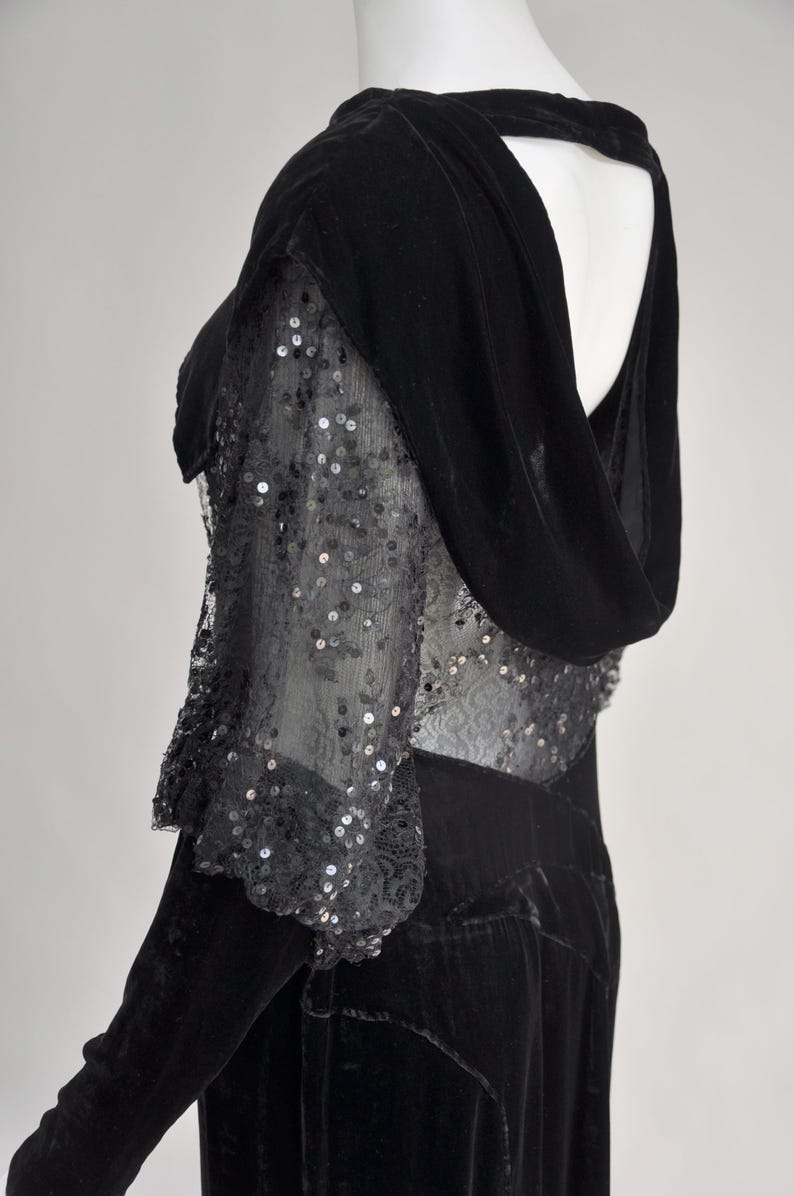 Puede incluir: Vestido negro de terciopelo con capucha y mangas transparentes con lentejuelas. Las mangas est&aacute;n adornadas con encaje. El vestido tiene una silueta larga y ajustada y una espalda recortada. El estilo es vintage y elegante.