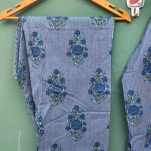 以下が含まれることがあります： 青と白のストライプのパジャマパンツ、花柄、木製のハンガーに吊るされています。パンツは青い花と葉の繰り返し模様が特徴です。裾には白い縁取りがあります。