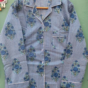 以下が含まれることがあります： 青と白のストライプのパジャマセット、花柄。長袖トップスはボタンダウンフロント、胸ポケット、白いトリム付き。花柄のデザインは青とティール色です。