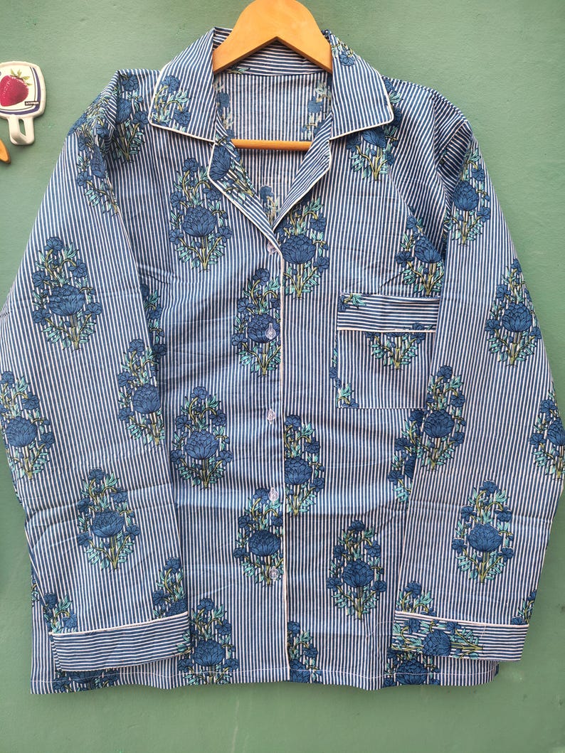 以下が含まれることがあります： 青と白のストライプのパジャマセット、花柄。長袖トップスはボタンダウンフロント、胸ポケット、白いトリム付き。花柄のデザインは青とティール色です。