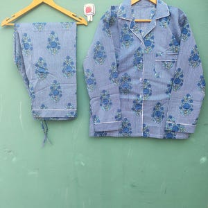 以下が含まれることがあります： 青と白のストライプのパジャマセット、花柄。 セットには、胸ポケット付きのボタンダウンシャツとパンツが含まれます。 パジャマは、緑色の背景に木製のハンガーに吊るされています。