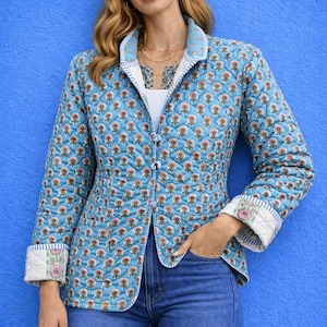 Könnte beinhalten: Gesteppte Jacke mit floralem Muster auf hellblauem Hintergrund. Die Jacke hat einen Kragen, einen Knopfverschluss und umgeschlagene Manschetten. Das Blumenmuster umfasst rosa und orangefarbene Blüten. Das Model trägt eine blaue Jeans.