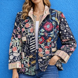 Może przedstawiać: Pikowana kurtka z żywym kwiatowym wzorem w kolorze czerwonym, różowym i zielonym na granatowym tle. Kurtka ma stójkę i jest połączona z niebieskimi dżinsami. Mankiety i kołnierz mają wzorzyste wykończenie.