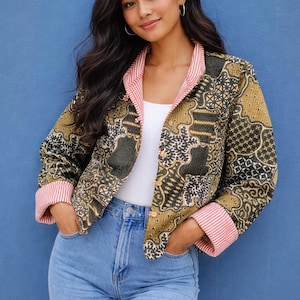 Puede incluir: Chaqueta estampada con forro y puños a rayas rojas y blancas. La chaqueta tiene un diseño dorado, negro y blanco y se combina con unos vaqueros azules. La modelo lleva un top blanco.