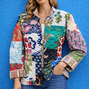 Può includere: Giacca trapuntata con un design patchwork con motivi floreali, animali e geometrici in vari colori. La giacca ha una cerniera dorata e viene indossata con jeans blu. Lo sfondo è un muro blu.