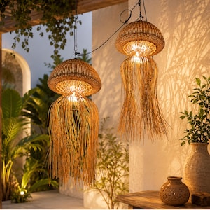 May include: Two pendant lights with a woven, mushroom-shaped design. The lamps are made of natural-colored wicker and have long, fringed strands hanging below. The lights are suspended from a dark cord and illuminate a warm, inviting glow.