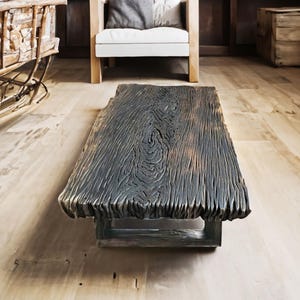 Könnte beinhalten: Ein rechteckiger Couchtisch aus dunklem, strukturiertem Holz. Der Tisch hat eine natürliche, rohe Kante und steht auf einem einfachen Untergestell. Die Holzmaserung ist deutlich sichtbar. Ungefähre Abmessungen: 150 cm x 75 cm.