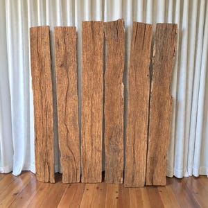 Pode incluir: Seis tábuas de madeira reciclada com aparência natural e desgastada. As tábuas estão na vertical, mostrando os veios e nós da madeira. A cor é marrom quente, com variações de tons. As tábuas variam em largura e comprimento, para decoração rústica.